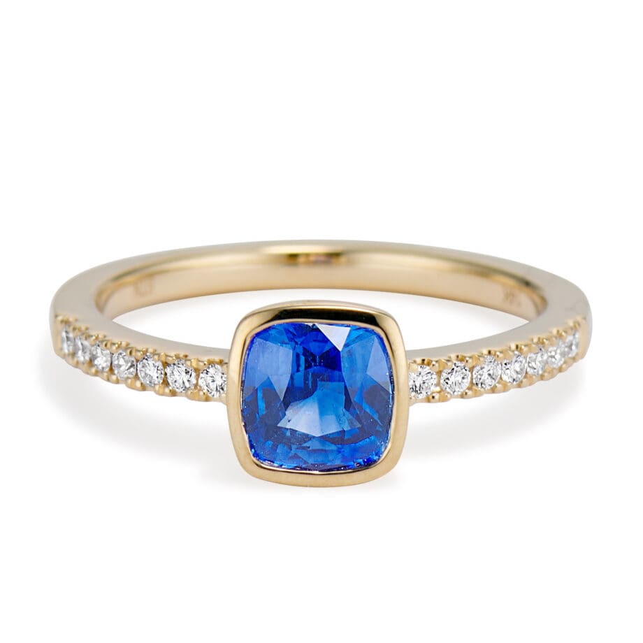Cushion Cut Blue Sapphire and Diamond Ring. bezel set sapphire and bead set diamond sides. straight on view