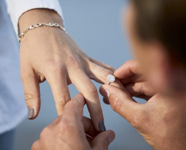 Man placing wedding band or engagement ring on woman's hand