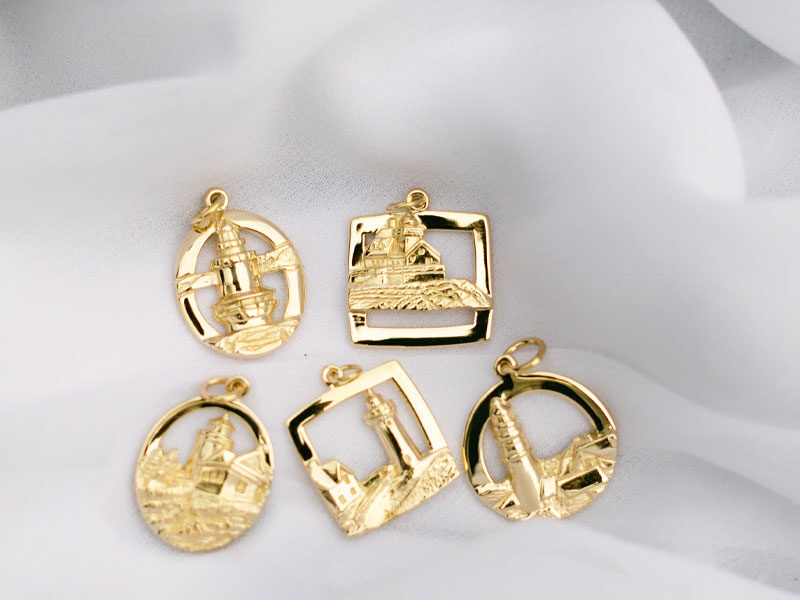 Gold charms of Maine lighthouses on white fabric background