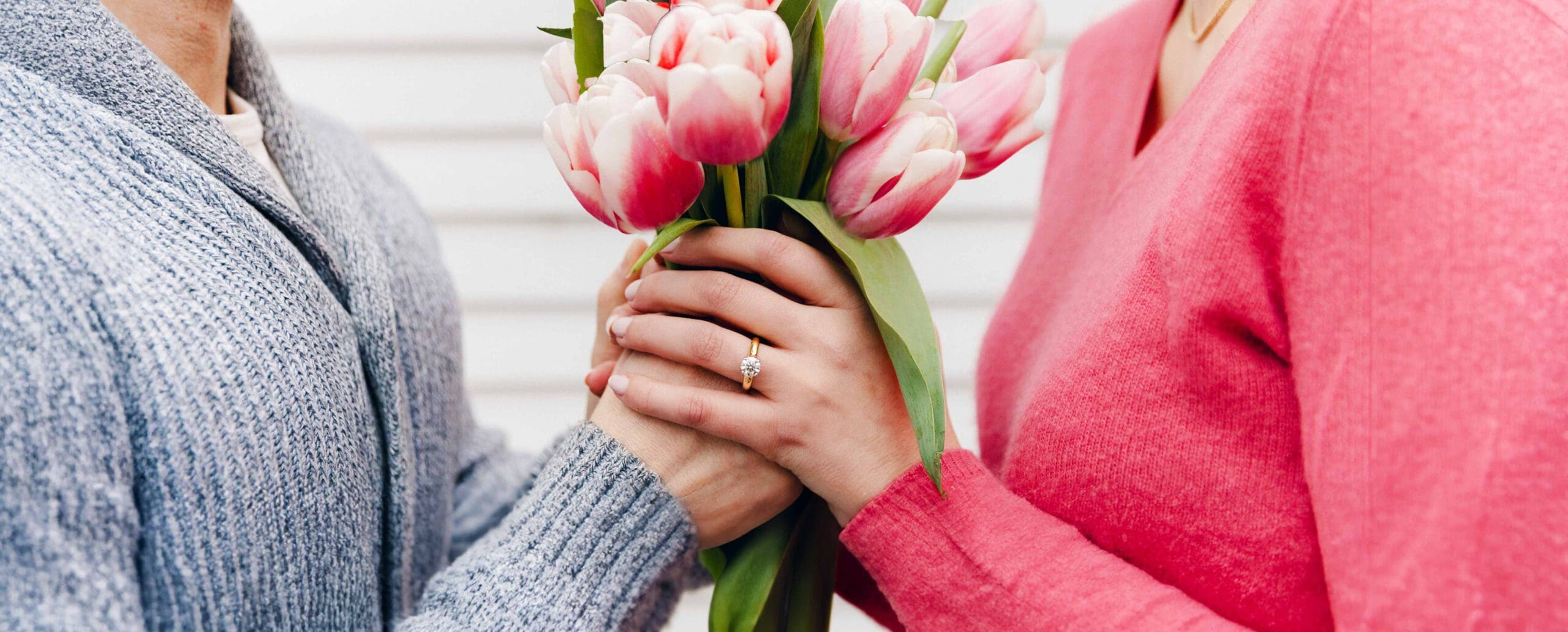 Spring Engagement man and women hands holding tulip bunch with a diamond classic yellow gold engagement ring on her left ring finger