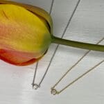 Graduation gift ideas. Diamond solitaire bezel Pendant Necklaces in yellow gold and 1 in white gold shown with a tulip
