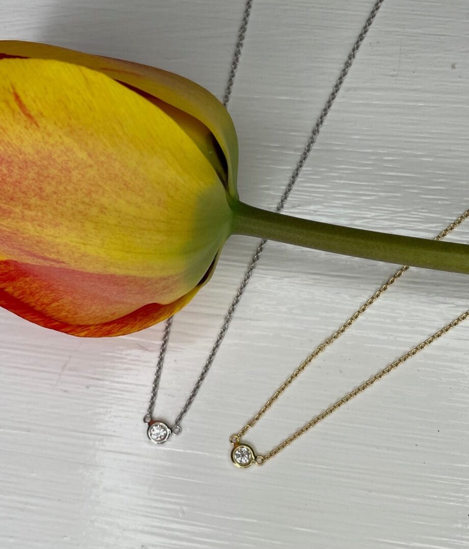 Graduation gift ideas. Diamond solitaire bezel Pendant Necklaces in yellow gold and 1 in white gold shown with a tulip