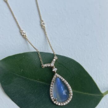 18K yellow gold necklace with a pear cut blue rainbow moonstone surrounded by a diamond halo on an adjustable diamonds by the yard chain