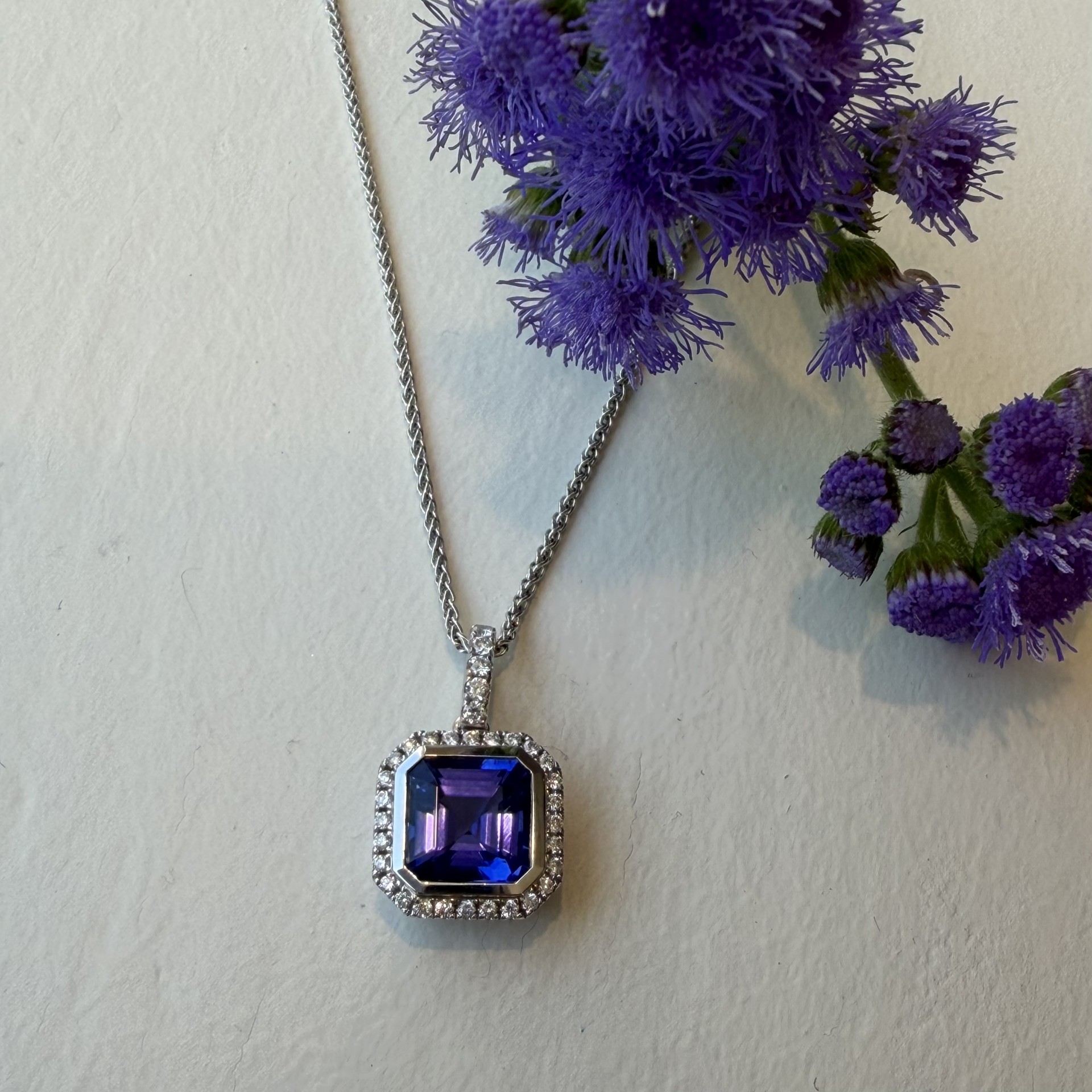 Bezel set tanzanite pendant with diamond halo and bail in 14K white gold